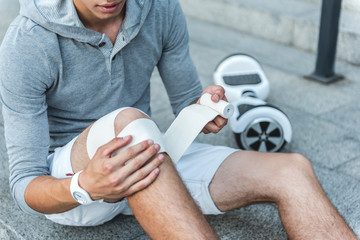 Male bandaging leg on floor outdoor