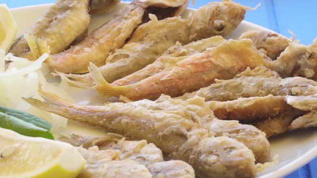 Plate of fried small fish red mullet with arugula and lemon, close up view.