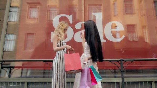 Cheerful Beautiful Girlfriends Discussing Shopping at the Window With a Sale