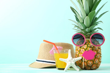Ripe pineapple with sunglasses and glass of juice on mint background