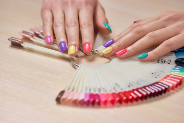 Obraz na płótnie Canvas Multicolored summer manicure on female hands. Beautiful pastel manicure on young womans hands, palettes with nail polishes. Salon beauty and spa.