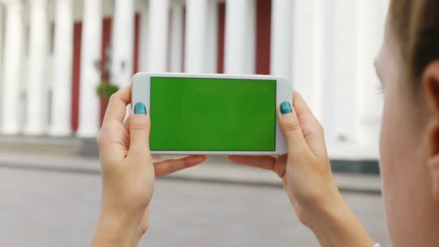 Closeup woman girl hands holding horizontal white smart phone mobile city urban old building blur background green screen chroma key digital gadget application taking picture 3g online connection