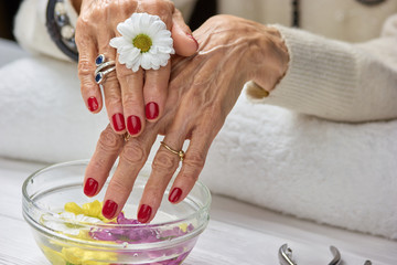 Woman with manicure in spa salon. Female hands with bowl of aroma spa water on table. Woman hands in nail salon receiving hands scrub peeling by beautician.