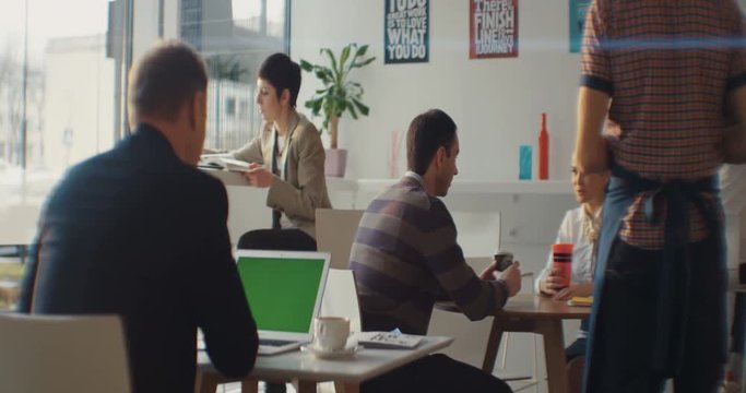 A man sitting in a cafe uses a laptop with a green screen. Around the people. The waiter accepts the order. Communication, Internet, online, meeting, business plan, project. Shot on RED Epic Camera.