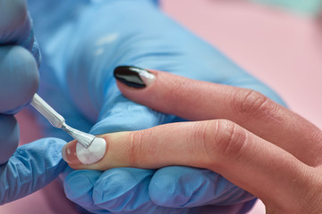 Manicurist painting nails to client. Manicure master applying white nail varnish on clients nails at nail salon. Nail care and treatment.