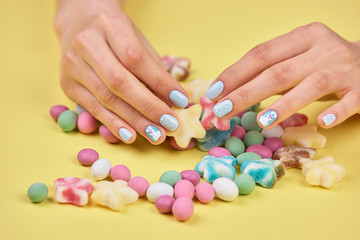 Obraz na płótnie Canvas Colorful candies in womans hands. Womans hands with bright manicure taking a colorful candy, yellow background.