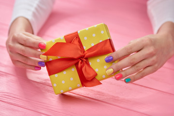 Female hands and yellow gift box. Female beautiful hands holding gift box close up, wooden background.