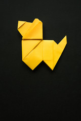 Yellow folded origami dog on black paper background. Vertical holiday postcard, poster, banner template. Empty space for copy, text, lettering.