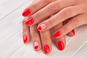 Female hands with polished nails. Woman gentle hands with red hearts and dots design manicure on white wooden background close up.