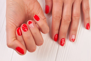 Caucasian woman manicured hands. Valentines Day Holiday bright manicure with painted hearts and dots. Female winter manicure on Valentine Day.