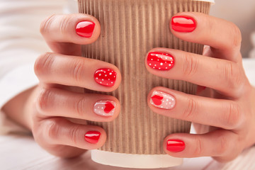 Disposable coffee cup in female hands. Woman hands with beautiful manicure holding cardboard cup with cappuccino close up.