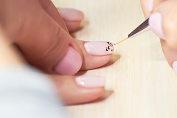 Manicurist drawing on female nails. Nail beautician making a draw on clients nails in beauty salon....
