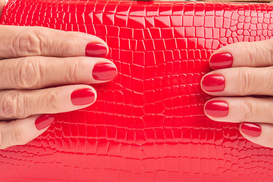 Close up red leather purse in female hands. Woman hands with red manicure holding red lacquered handbag close up.