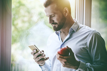 handsome businessman using smart phone and eating apple