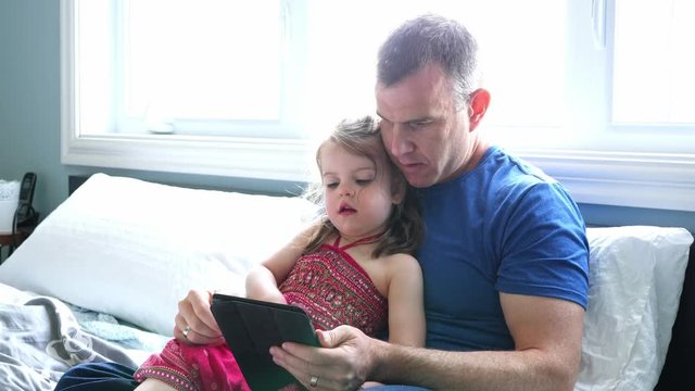 father and daughter relax in bed with tablet computer