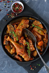 Chicken stewed with vegetables and tomato on a stone board in a frying pan.