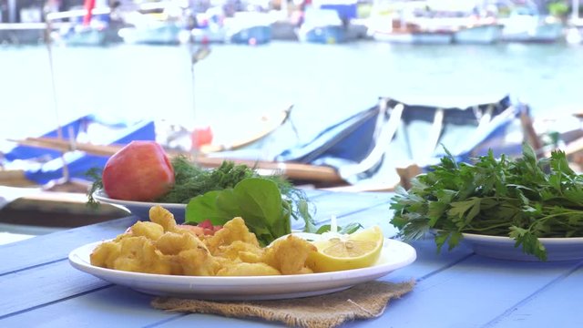 Fried seafood with lemon and arugula on blue table by the sea and small boats at small town.