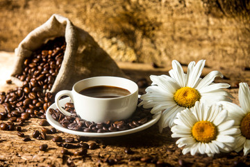 Coffee cup and fried coffee beans on a wooden table with beautiful white flowers on a wood background