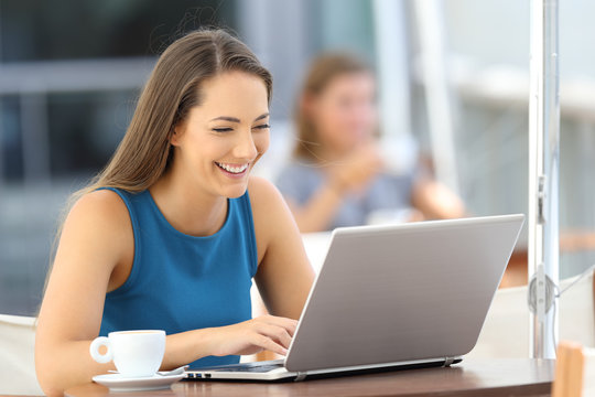 Happy woman using a laptop in a bar terrace