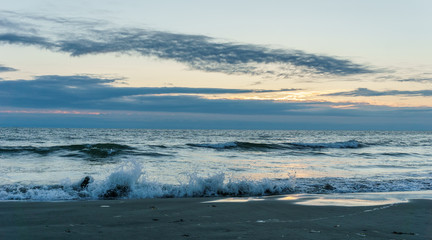 Sunset on ocean shore waves on water.