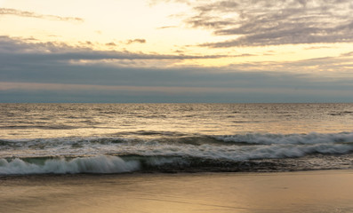Sunset on ocean shore waves on water.
