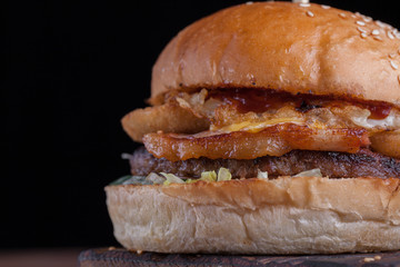 Closeup of a juicy Burger with bacon, fried onion rings and cheese on dark wooden background.