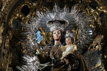 Close-up of traditional procession statue of Madonna and the Child in church of Sevilla, dressed in black, white and silver with some baroque ornaments in behind