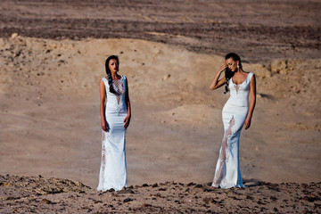 Fototapeta na wymiar Two girls in white dresses posing in sand dunes