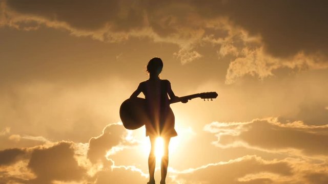 A silhouette of the girl against the sky. A girl is playing the guitar. Beautiful sunset. Backlight.