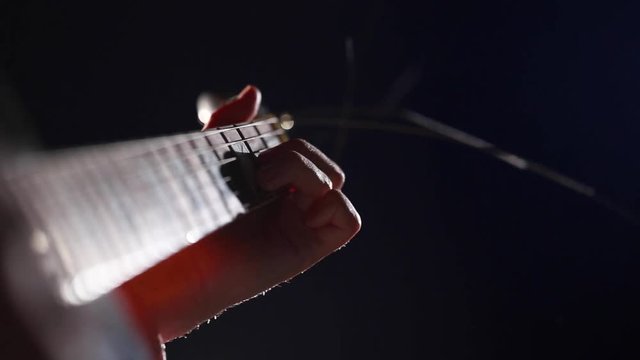 The hand of the musician on the guitar fretboard over closeup