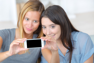 happy teen girls sitting on sofa and taking selfie