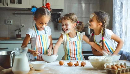 Photo sur Aluminium Cuisinier happy sisters children girls bake cookies, knead dough, play with flour and laugh