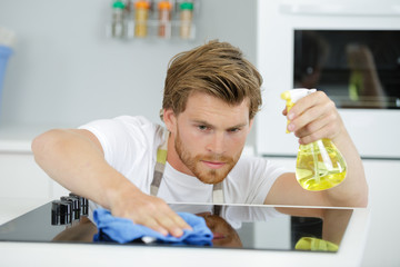 male cleaning kitchen with detergent spray bottle and sponge