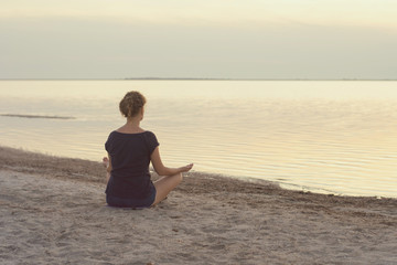 Fototapeta na wymiar A girl sits on the lake shore and meditates in the evening