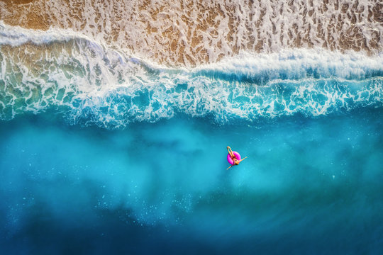 Aerial view of slim woman swimming on the pink swim ring in the transparent turquoise sea in Oludeniz,Turkey. Summer seascape with girl, beautiful waves, colorful water at sunset. Top view from drone