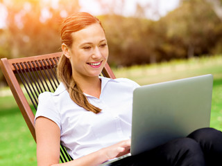 Young business woman sitting in park and working with laptop