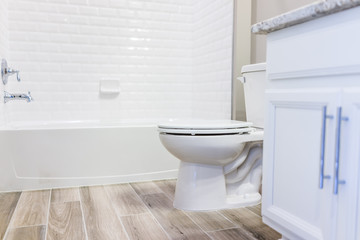 Naklejka na ściany i meble Modern white plain clean toilet bathroom, bathtub with shower tiles and hardwood floors with staging in model staging house, home or apartment