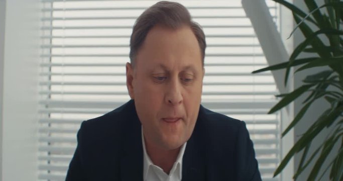 A serious businessman looks at the camera and speaks to the camera in the office. Shot on RED Epic Camera.