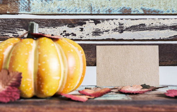 Thanksgiving and autumn concept of blank brown paper tag and pumpkin with maple leaves on wood chair
