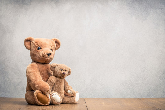 Two retro plush Teddy Bear toys family: parent with baby front concrete wall background. Parenthood concept. Vintage instagram old style filtered photo