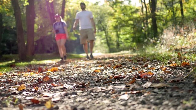 Couple walks down through a nature trail towards the camera in autumn