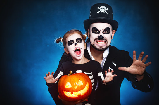 family father and daughter in costumes and make-up to Halloween with pumpkin