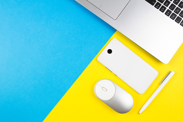 Modern workplace with notebook, computer mouse, mobile phone and white pen on blue and yellow color background