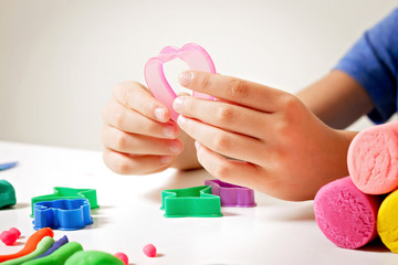 Child hands playing with modeling clay or plasticine on white table