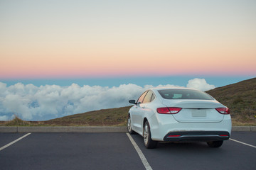 White car in mountains above the clouds at sunset or sunrise