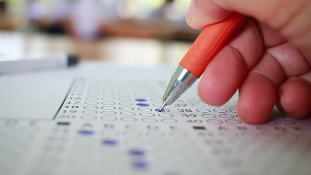 Asian Students holding pencil in hand doing multiple-choice quizzes or testing exams answer sheets exercises on old wood table In blur student school, college university classroom in education concept