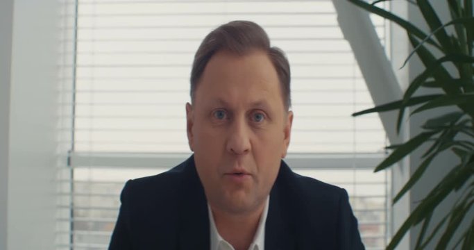 A serious businessman looks at the camera and speaks to the camera in the office. Manager, business coach. Shot on RED Epic Camera.