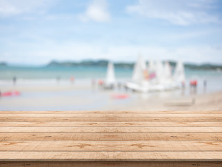 Empty wooden table in front with blurred background at the beach and sailboat,space for montage you products