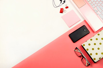 Woman's workplace with pink laptop, notebook, phone, glasses, paper notes, binder clips and headphones. pastel pink and white. Flat lay.