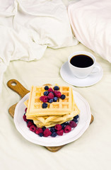Waffles with berries and coffee on a bed, concept of breakfast in bed. Selective focus